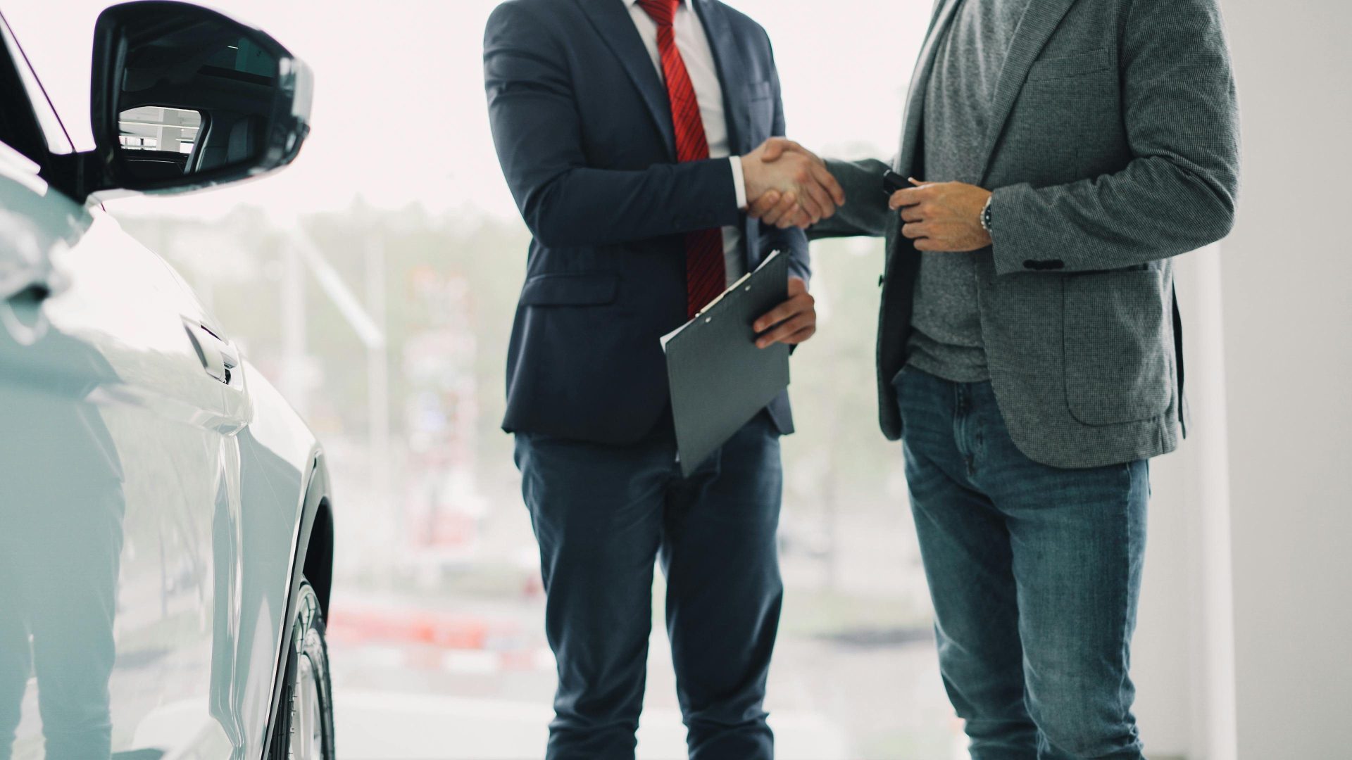 Zwei Männer besiegeln mit einem Handschlag in einem Autohaus ein Geschäft.