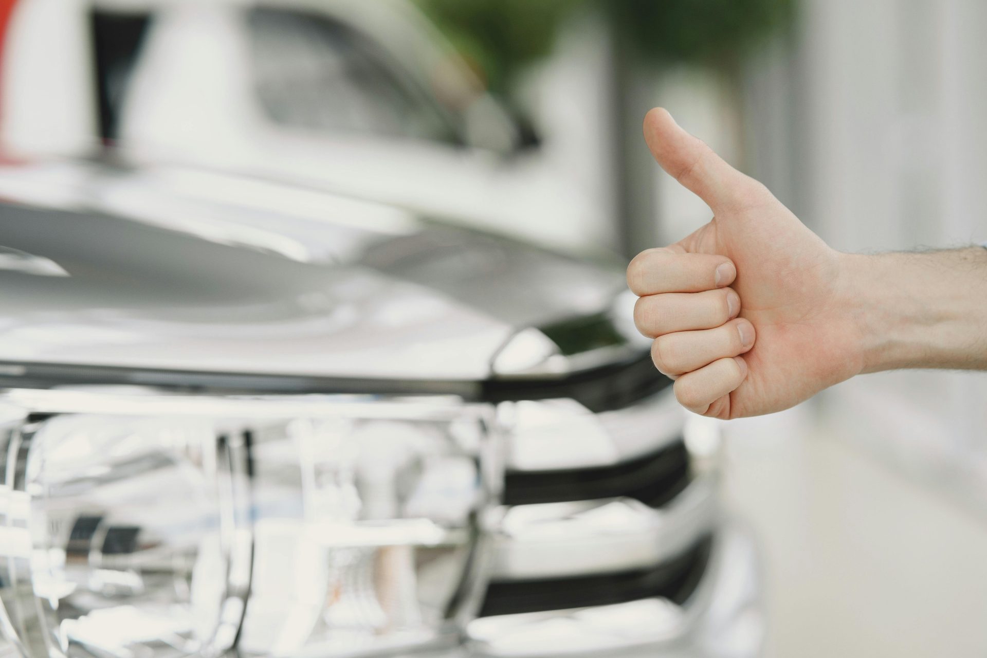 Nahaufnahme eines erhobenen Daumens neben einem Autoscheinwerfer, der Zustimmung oder Zufriedenheit symbolisiert.