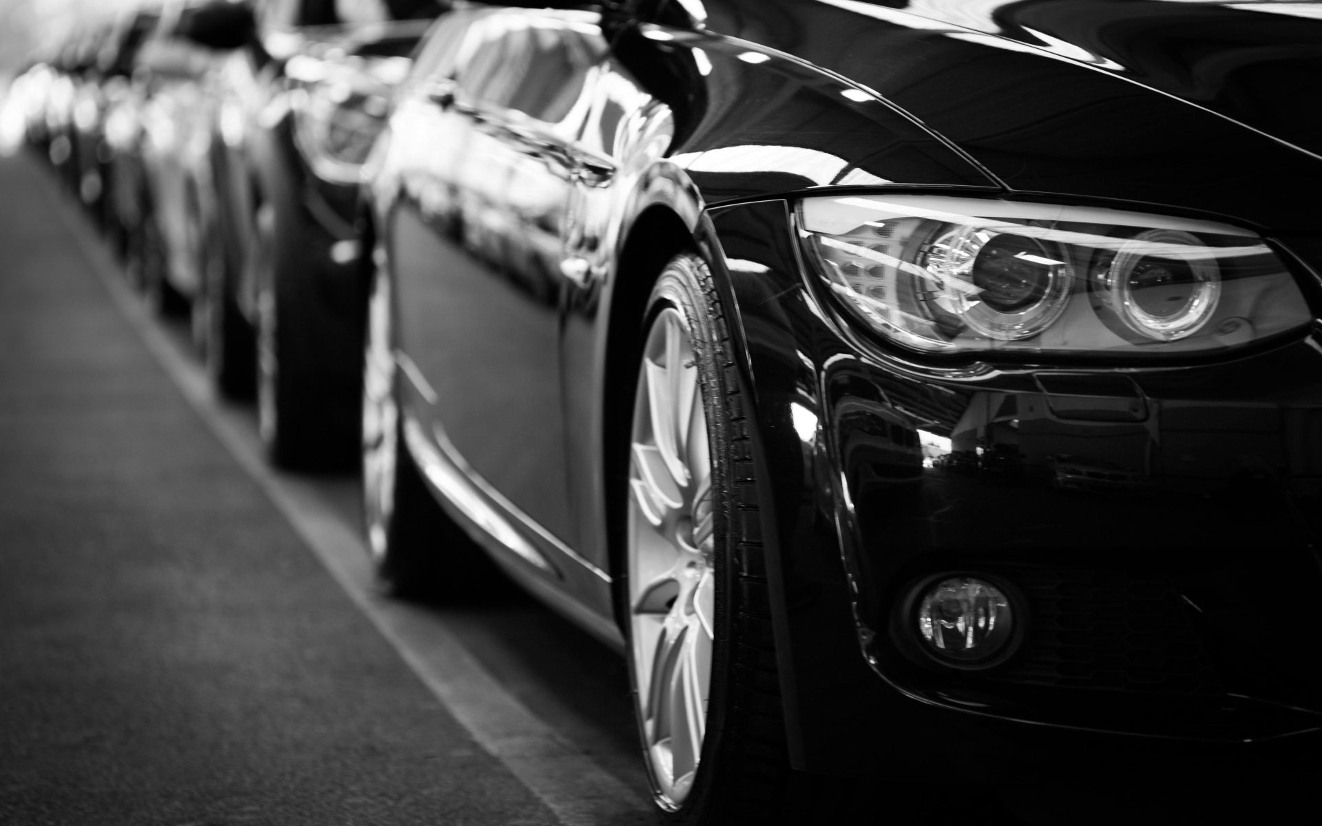 Nahaufnahme in Schwarzweiß von einer Reihe von Luxusautos mit Fokus auf die Fahrzeugscheinwerfer.